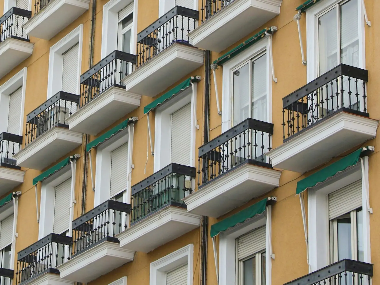 Fachada de un bloque de viviendas con balcones de forja, persianas y toldos